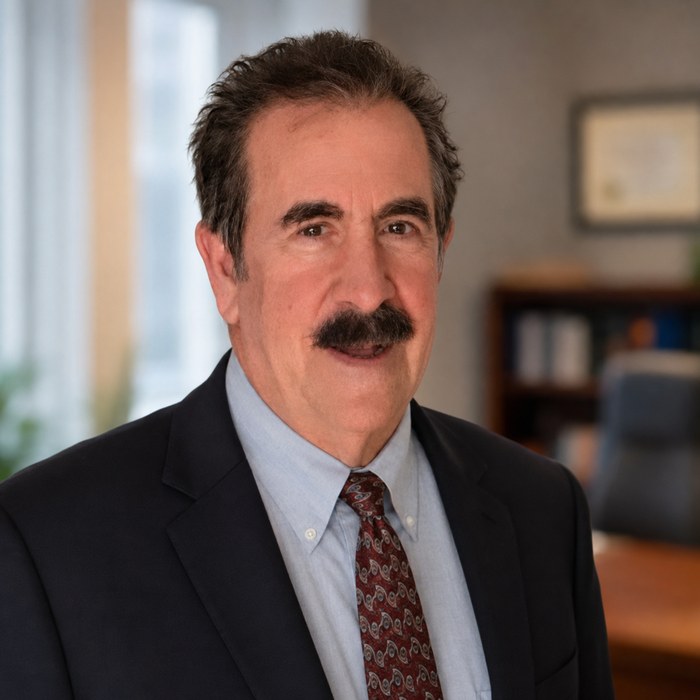 David C. Petrone, Esq., photographed in an office. He has dark greying hair and a moustache and wears a navy suit, a pale blue shirt and a patterned burgundy tie.