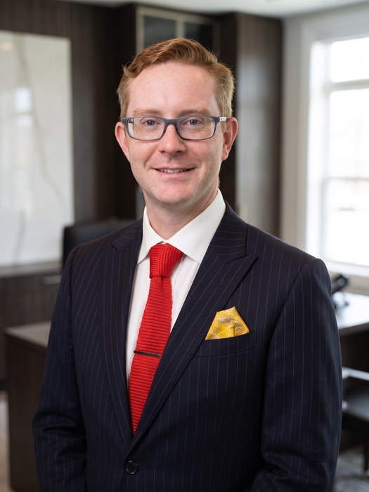 Laurence P. Banville, Esq., photographed in an office. He has short reddish-blond hair and rectangular glasses, and wears a navy pinstripe suit, a white shirt and a red knitted tie.